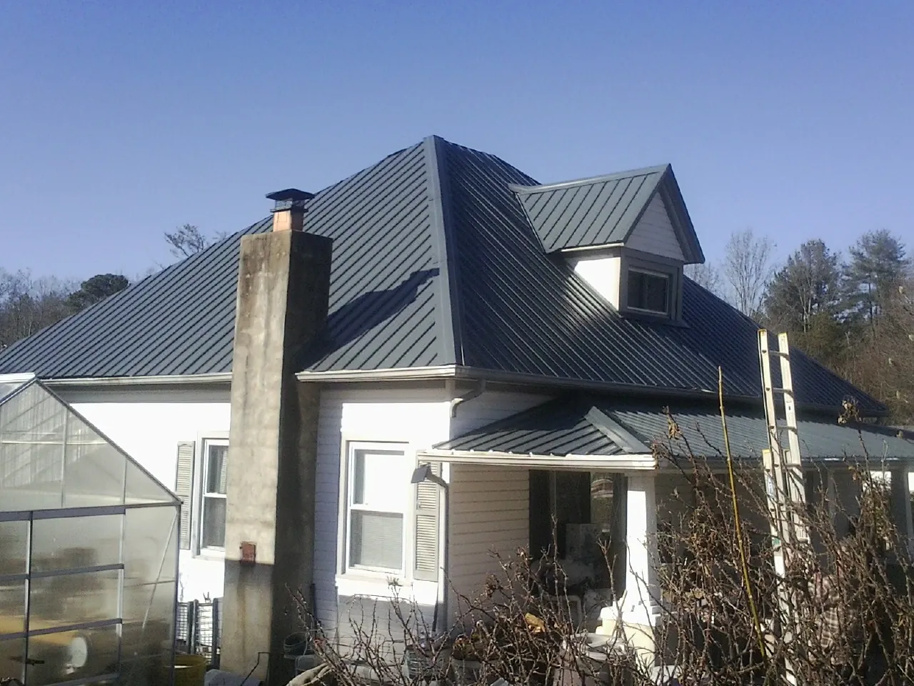 Dark blue standing seam metal roof on a white farmhouse with dormer — Slate & Tile Roof Repair by Roofing Brothers in Galva