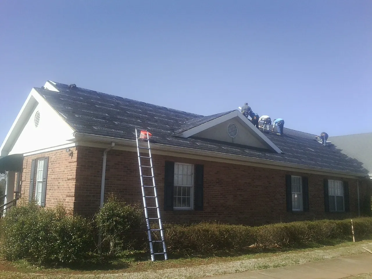 Crew tearing shingles off a brick ranch roof with a ladder set — Emergency Roof Repair work by our crew in Galva