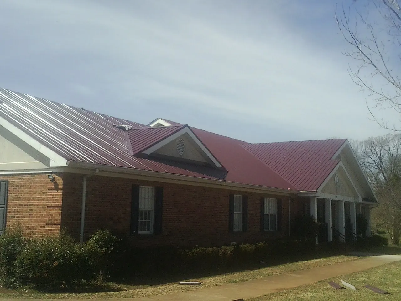 Red metal roof with gabled entries on a long brick building, from a Hail Damage Roof Repair job in Galva