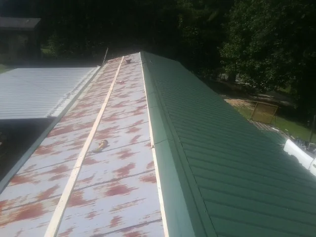 Old rusted panels beside newly installed green metal roofing — Wind Damage Roof Repair by Roofing Brothers in Galva