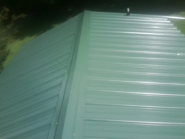 New green metal panels meeting at the ridge of a roof — Flat Roof Repair work by our crew in Galva