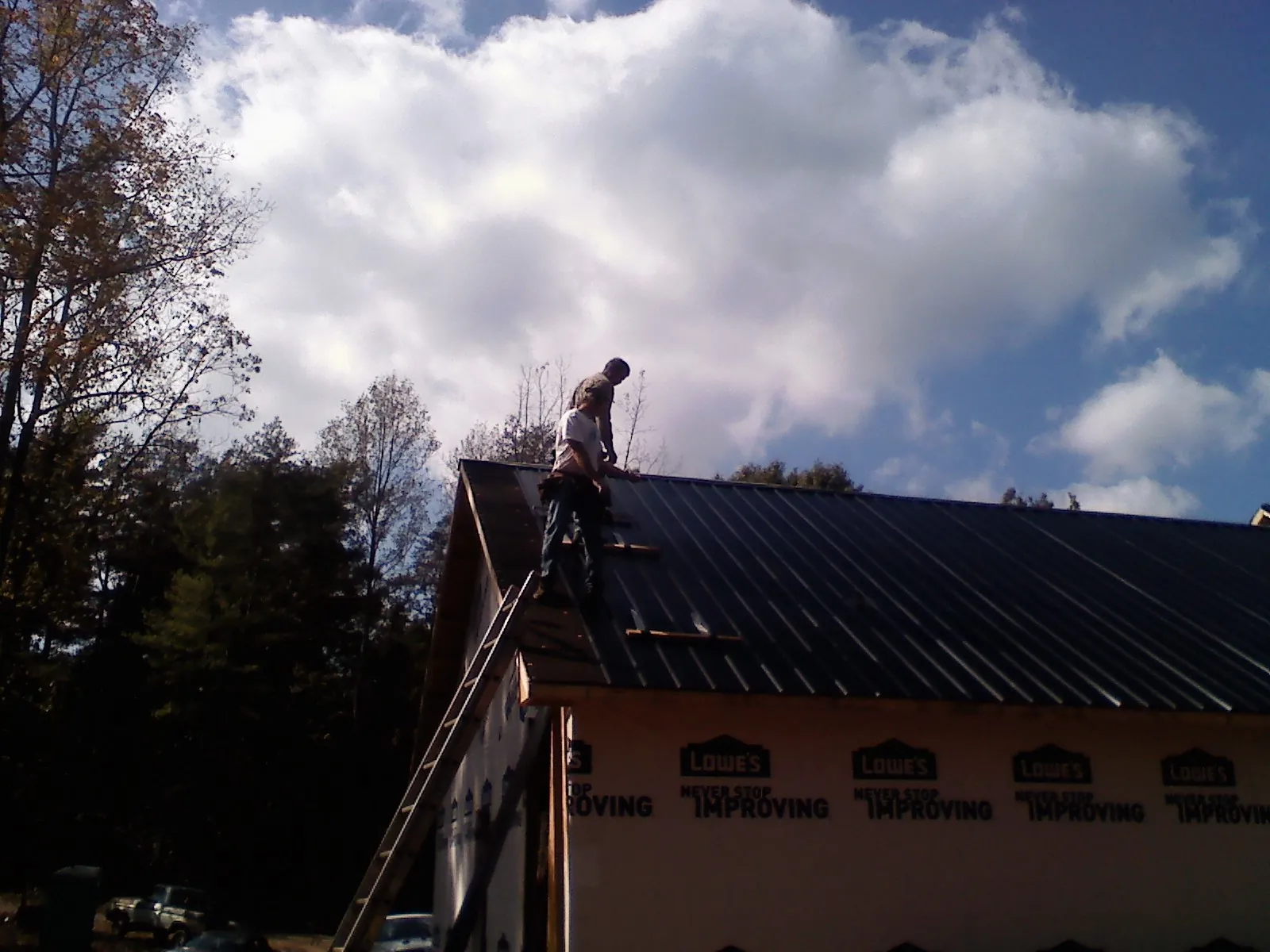 Roofer fastening dark metal panels high against a cloudy sky, from a Roof Inspection job in Galva