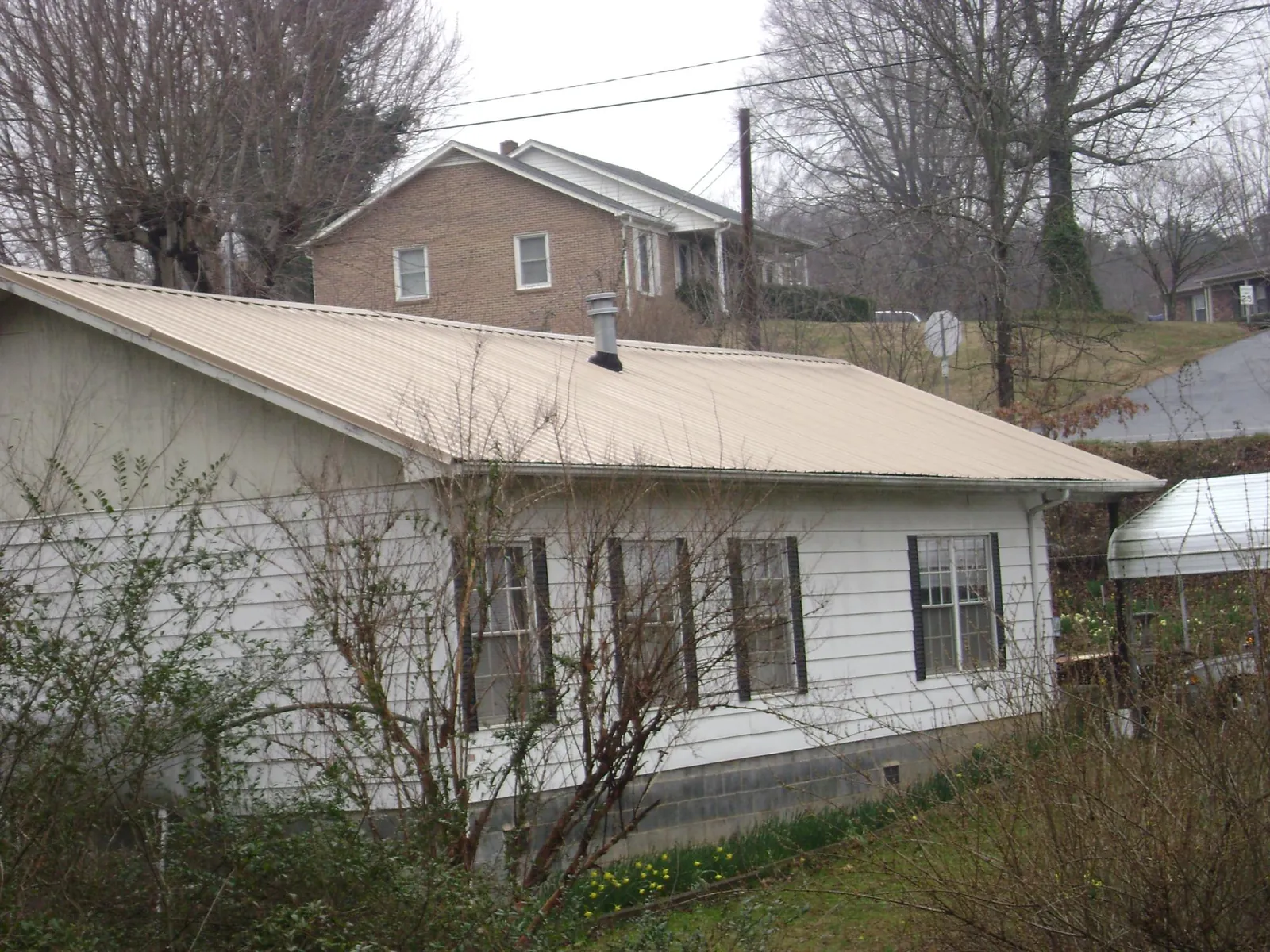 Tan metal roof on a white sided house set into a hillside — Commercial Roofing by Roofing Brothers in Galva